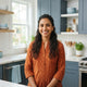 A friendly South Asian woman smiling in a bright, modern kitchen setting.